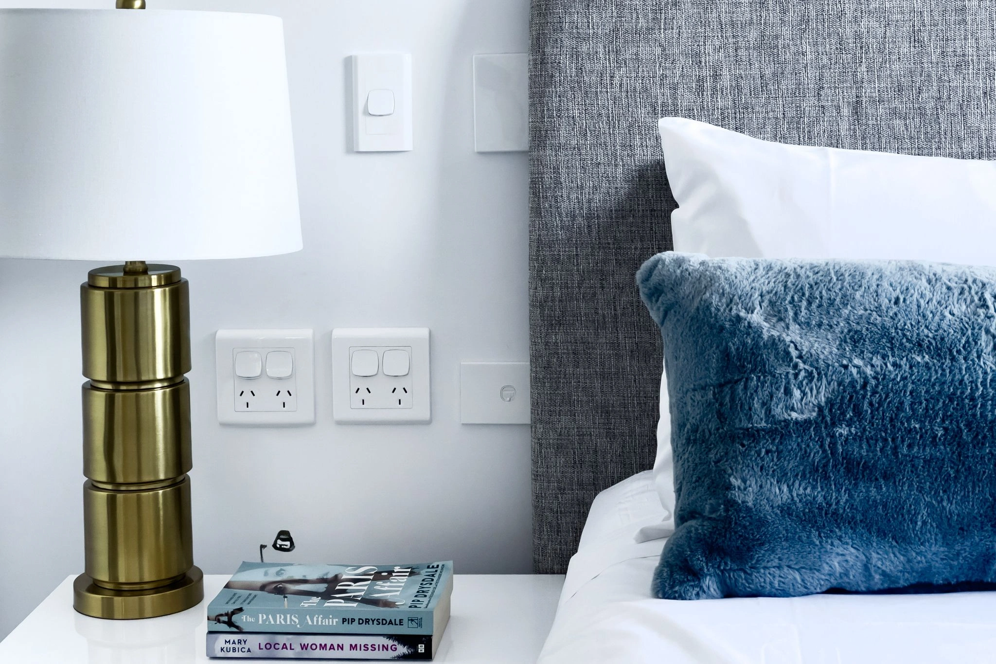 a bed with a blue pillow and a book on a table
